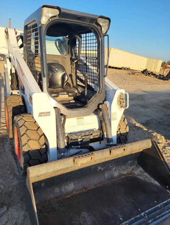 A mini skid steer maneuvering through a narrow space to remove yard waste.