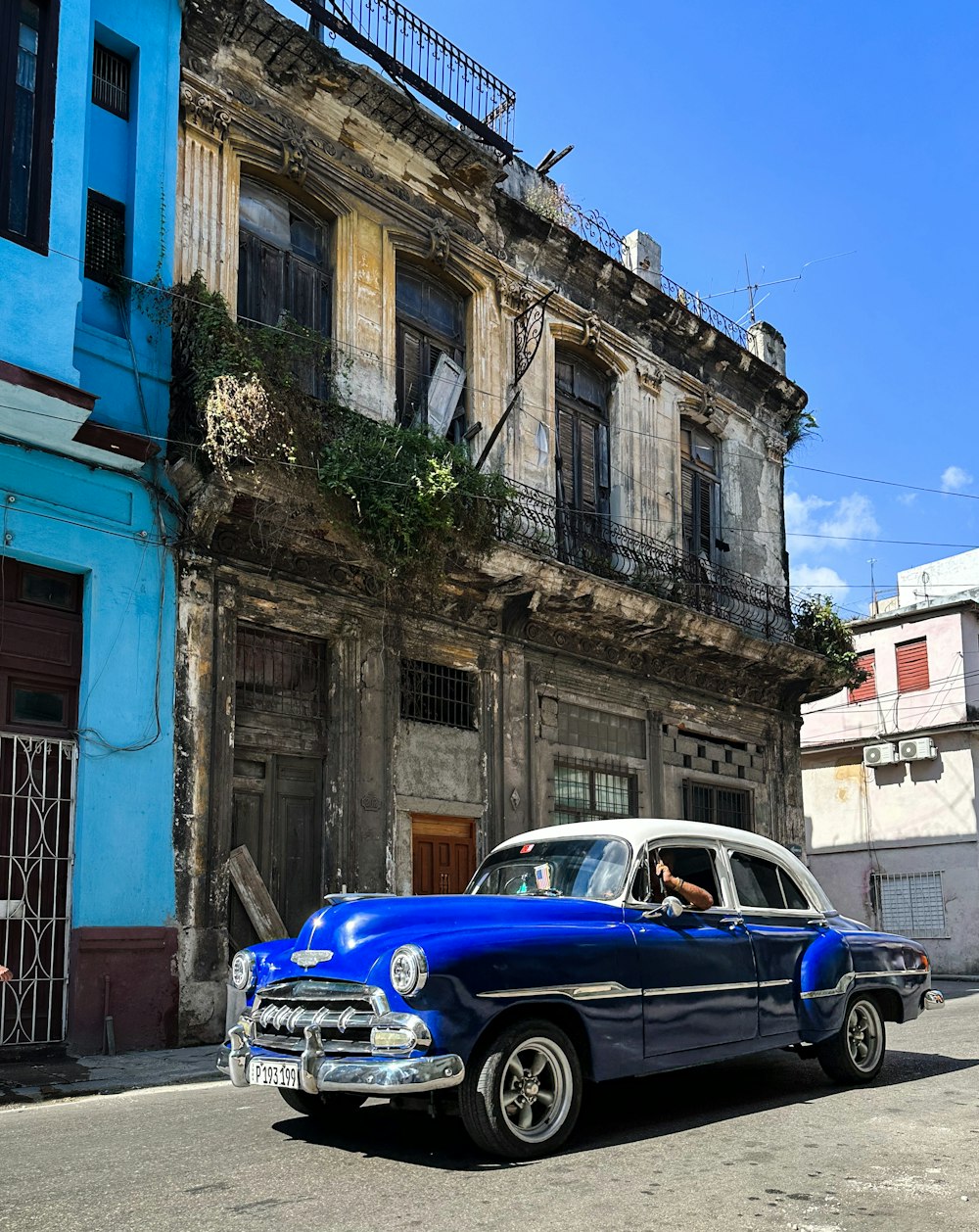 an old blue car parked in front of a building