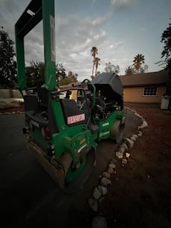 Heavy machinery compacting asphalt on a residential street surrounded by palm trees.