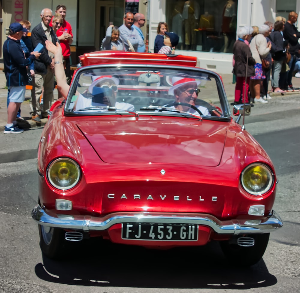 a red car driving down a street next to a crowd of people