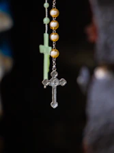 Close-up of a golden rosary resting on a black and gray textured surface with soft light highlighting the beads.