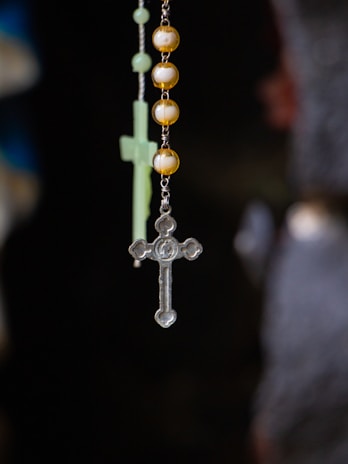 Close-up of a rosary held by a pilgrim with a scenic church background
