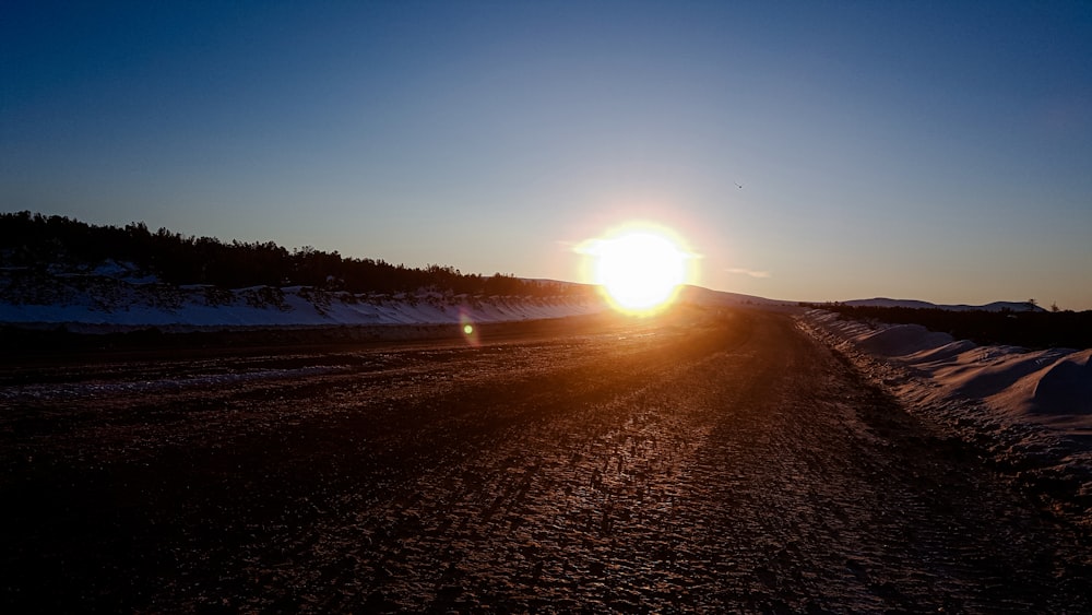 the sun is setting on a snowy road