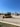 A construction equipment yard featuring several pieces of heavy machinery, including a large yellow bulldozer and an excavator under a clear blue sky. The ground is covered in gravel with a grassy edge in the foreground. In the background, there are more construction vehicles and a sign reading 'Holt CAT.'
