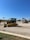 A construction equipment yard featuring several pieces of heavy machinery, including a large yellow bulldozer and an excavator under a clear blue sky. The ground is covered in gravel with a grassy edge in the foreground. In the background, there are more construction vehicles and a sign reading 'Holt CAT.'