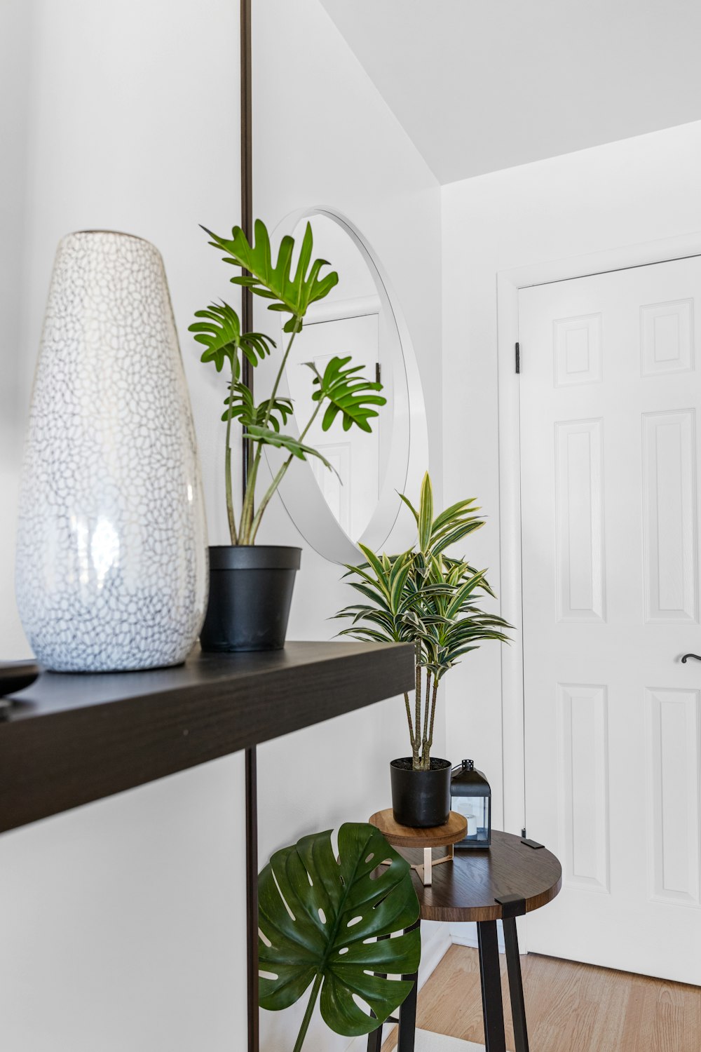 Un jarrón blanco sentado encima de un estante junto a una planta