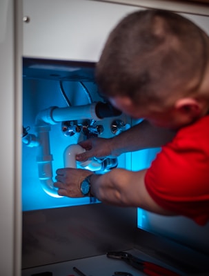 a man working on a pipe in a cabinet