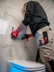 a man in a black shirt and red gloves working on a toilet