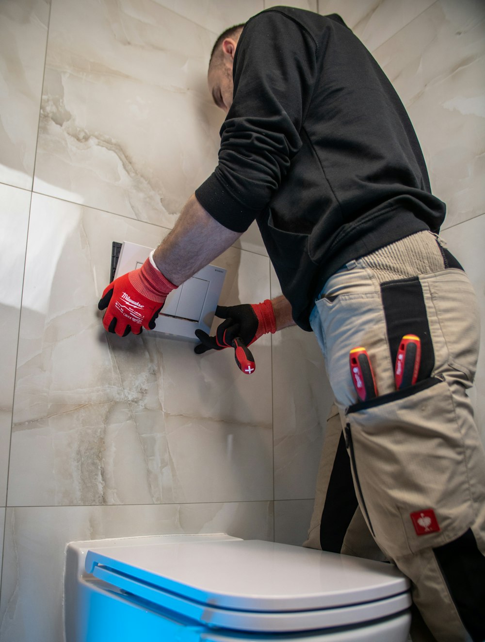 a man in a black shirt and red gloves working on a toilet