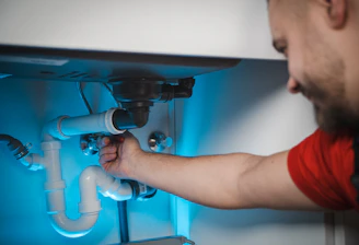A skilled plumber fixing a leaking pipe under a kitchen sink in a modern Riyadh home.