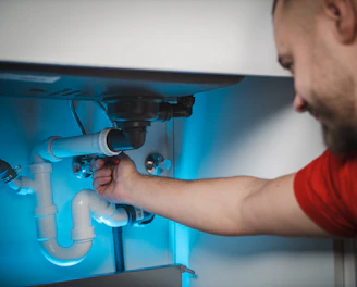 A professional plumber fixing a modern water pipe with blue and white tones in the background.