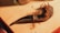 A wooden pipe with dried tobacco strands is placed on a wooden surface. The pipe has a textured, dark brown finish and a curved stem. Nearby, parts of glass jars are visible, suggesting a cozy setting.