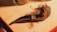 A wooden pipe with dried tobacco strands is placed on a wooden surface. The pipe has a textured, dark brown finish and a curved stem. Nearby, parts of glass jars are visible, suggesting a cozy setting.