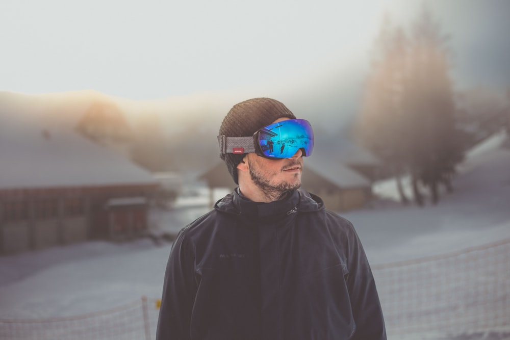 a man standing in the snow wearing a hat and goggles