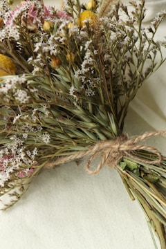 A rustic bouquet of wildflowers and native greenery wrapped in natural twine, set on a wooden table.