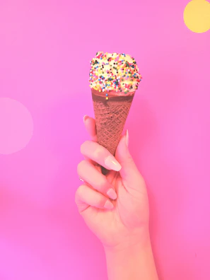 Close-up of a pastel pink ice cream cone with sprinkles on a sunny day