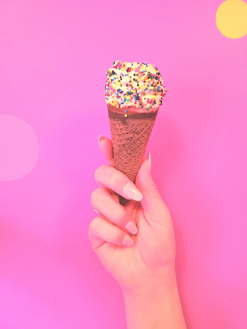 Close-up of a hand holding a cone of creamy ice cream with colorful sprinkles.