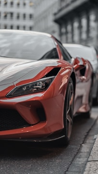 Close-up shot of a sleek red sports car reflecting sunlight on a city street.