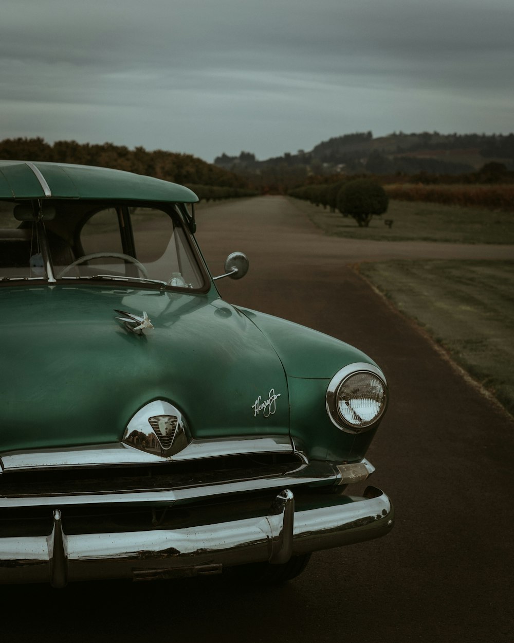 an old green car parked on the side of a road