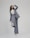 A person is shown in a dynamic pose, wearing a tailored blue-grey pantsuit and white high-heeled shoes. The background is minimalist and plain, emphasizing the fashionable nature of the outfit. The person is looking upward with a playful expression.