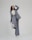 A person is shown in a dynamic pose, wearing a tailored blue-grey pantsuit and white high-heeled shoes. The background is minimalist and plain, emphasizing the fashionable nature of the outfit. The person is looking upward with a playful expression.