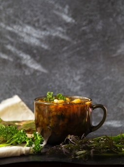 A rustic kitchen table with fresh herbs, colorful vegetables, and a steaming bowl of healing soup.