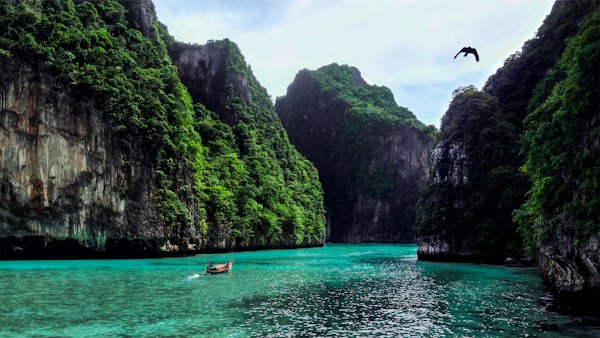 A person in a boat in a body of water surrounded by mountains — Koh Phi Phi, Thailand