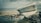 A damaged boat with the name 'ECEM' is stranded on a concrete surface near the edge of a body of water. Debris and pieces of wreckage are scattered around it, possibly from the boat or other structures. The sky is overcast, adding a gloomy atmosphere to the scene.