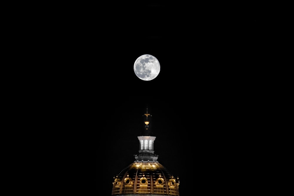 um edifício com uma torre do relógio e uma lua cheia ao fundo