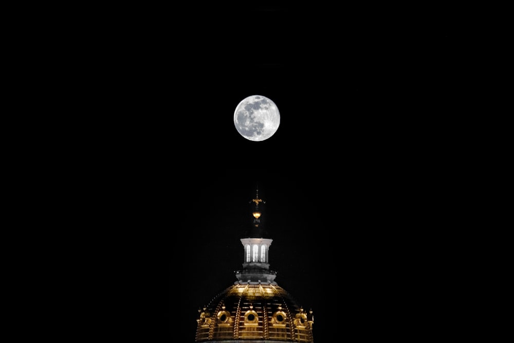 Un edificio con una torre del reloj y una luna llena al fondo