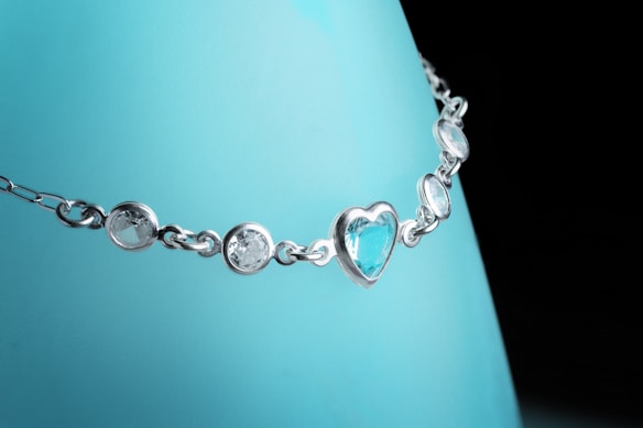 A delicate necklace featuring a silver chain with circular and heart-shaped blue gemstones, displayed against a light blue background.