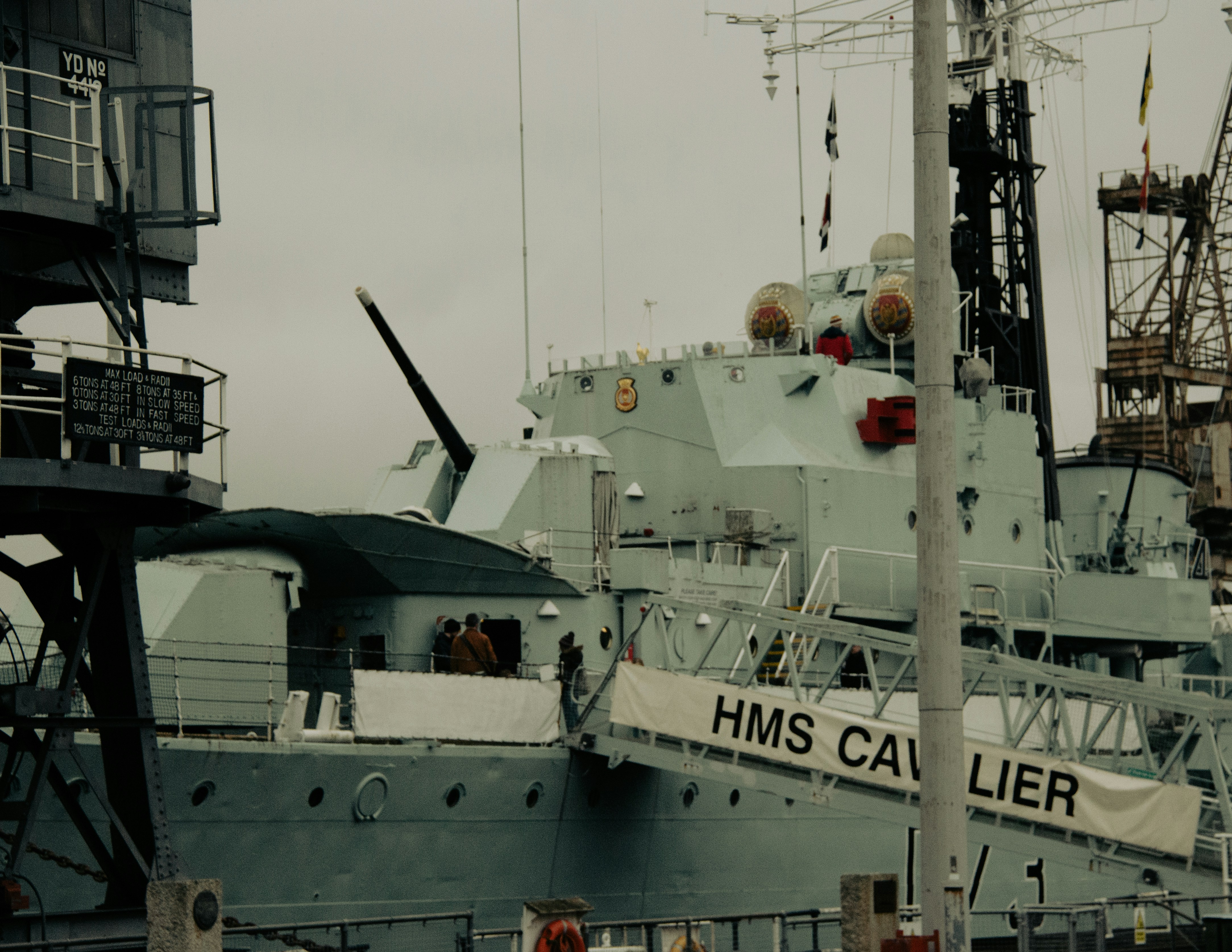 A military ship docked at a dock with a crane in the background