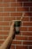 A hand holding a green disposable cup with a paper straw against a background of a red brick wall.