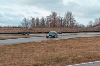 A driver practicing advanced car handling on a winding road surrounded by trees under a clear sky.