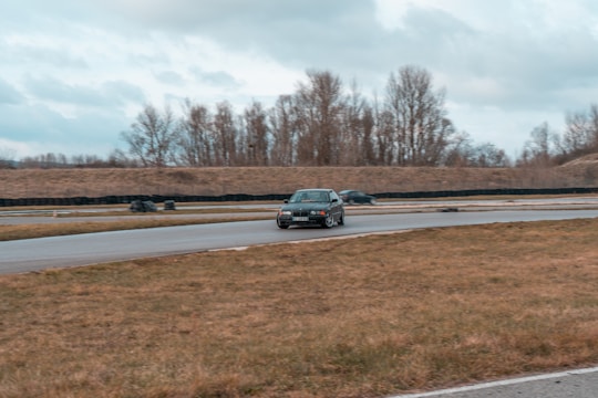 A driver practicing advanced car handling on a winding road surrounded by trees under a clear sky.