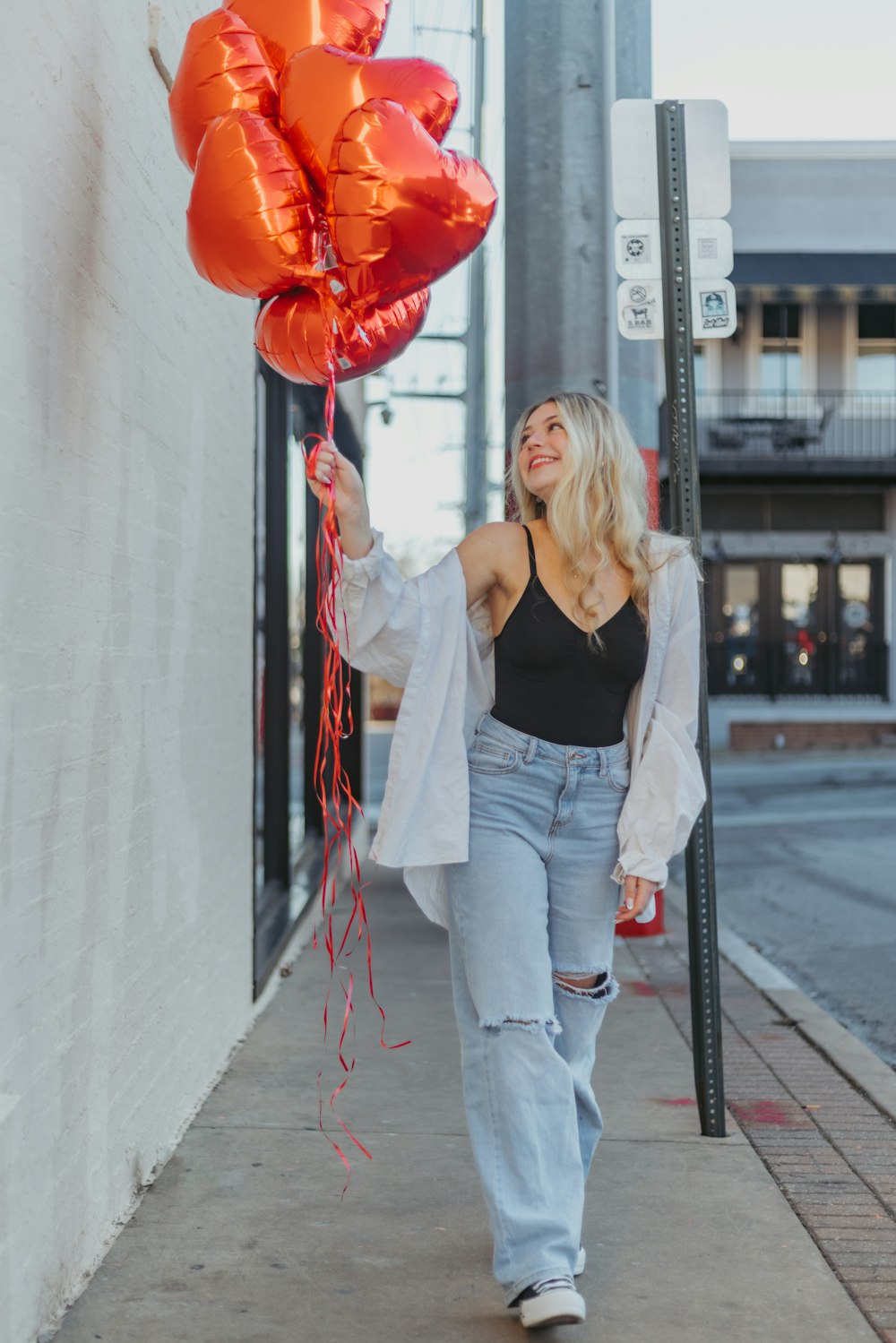 a woman walking down a sidewalk with a bunch of balloons