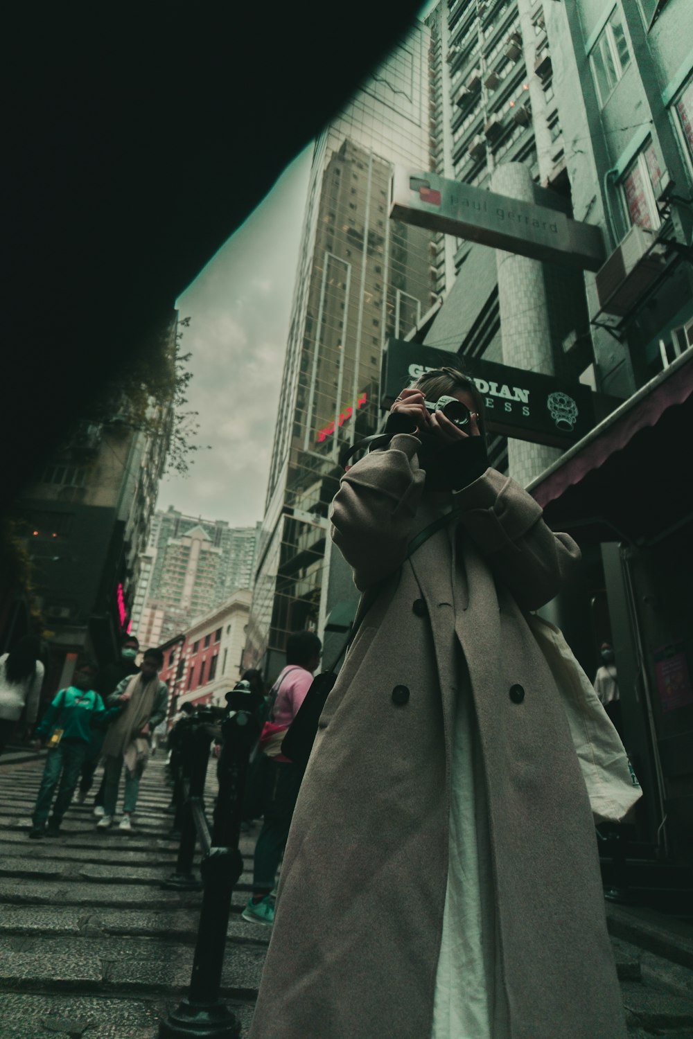 a woman in a trench coat is standing on a city street