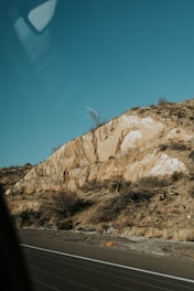 A geologist examining rock samples on a rugged hillside under a clear sky.