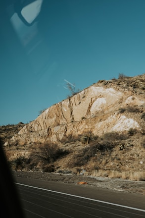 A geologist examining rock samples on a rugged hillside under a clear sky.