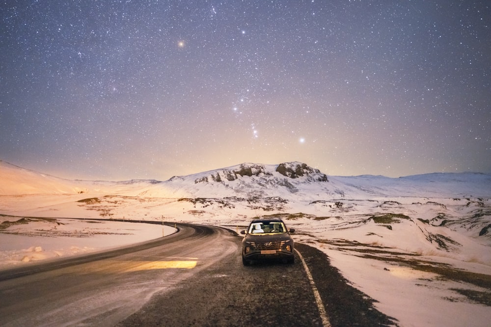 a car driving down a snowy road under a night sky