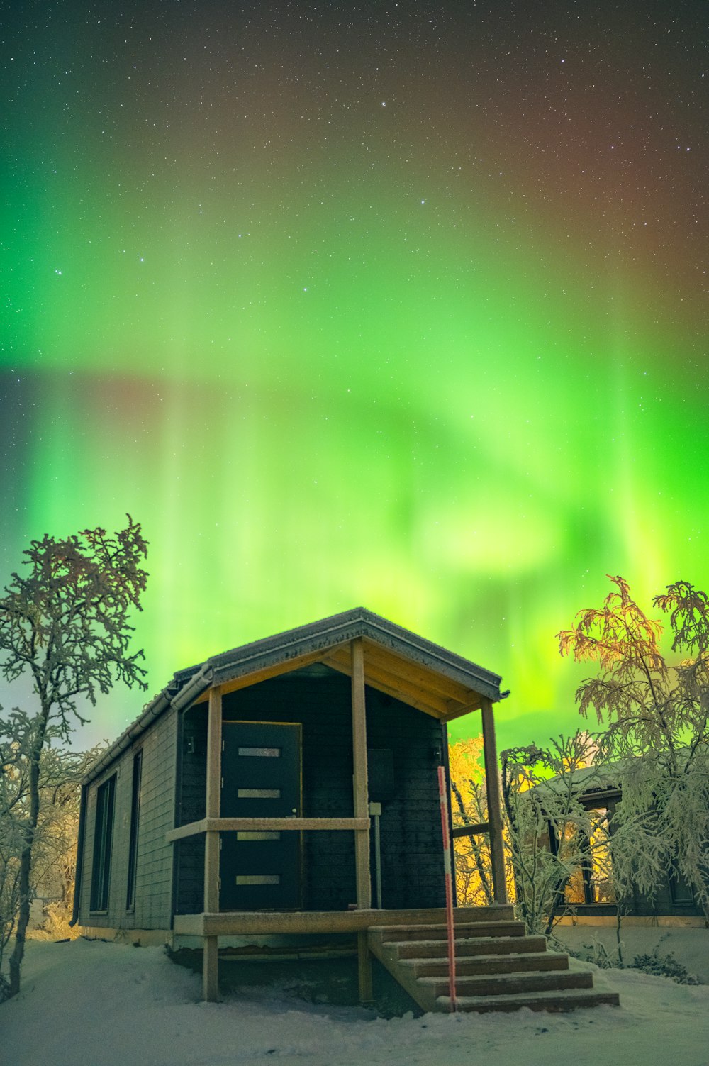 a small cabin with a green and red aurora light in the background