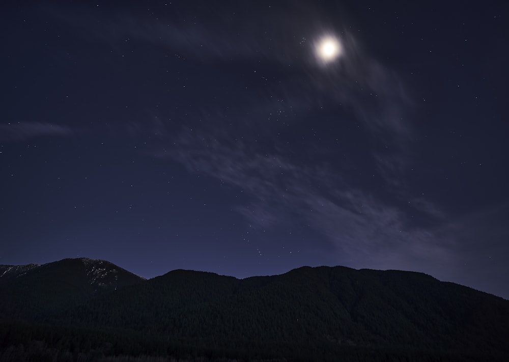 a full moon is seen above a mountain range