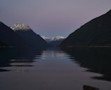 A serene alpine lake reflecting snow-capped mountains at dusk with photographers silhouetted along the shore.