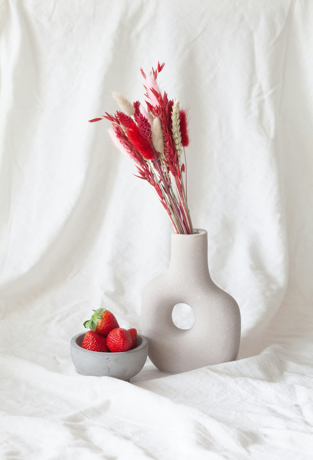 Un jarrón blanco sentado junto a un tazón de fresas