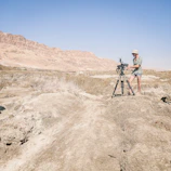 Wide shot of a desert landscape with a treasure hunter using a detector near rugged hills.