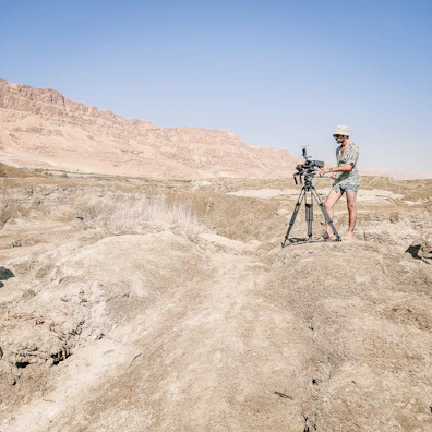 Wide shot of a desert landscape with a treasure hunter using a detector near rugged hills.