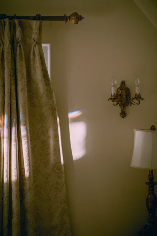A cozy living room corner featuring a vintage brass sconce casting warm light over a fabric wall tapestry with earthy tones.