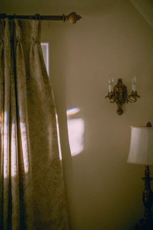 A cozy room corner showcasing elegant curtains and patterned wallpaper bathed in soft natural light.