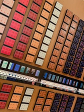 A neatly organized display of various coffee pods arranged in rows and columns on a wooden surface. The pods are housed in colorful packaging, varying from red, orange, and cream to darker shades. Below the pods, there are rows of capsules and promotional materials likely detailing different coffee flavors.