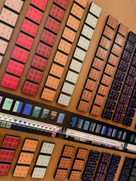 A neatly organized display of various coffee pods arranged in rows and columns on a wooden surface. The pods are housed in colorful packaging, varying from red, orange, and cream to darker shades. Below the pods, there are rows of capsules and promotional materials likely detailing different coffee flavors.